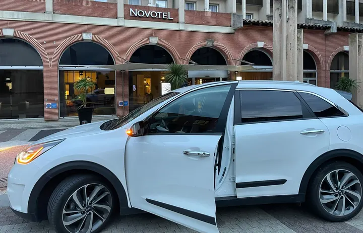 Chauffeure VTC à Toulouse : la Kia Niro de Louise, portière ouverte devant un hôtel